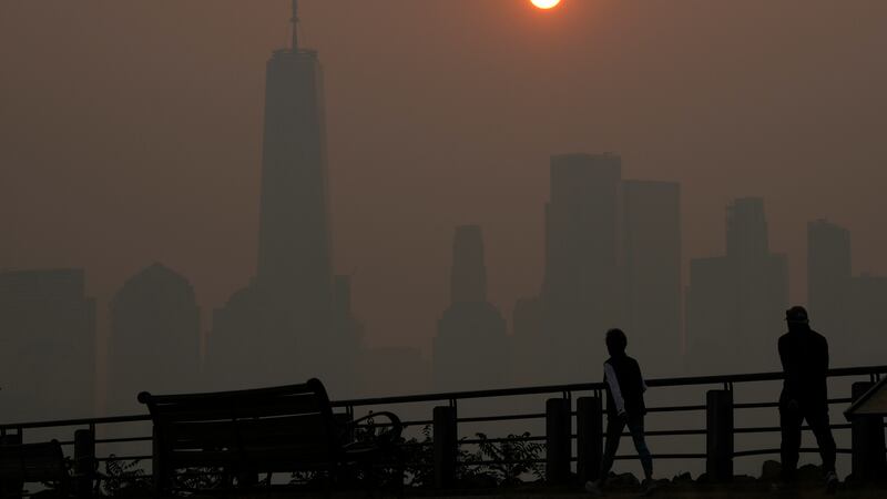 People walk in front of the sun rising over the lower Manhattan skyline in Jersey City, N.J.,...